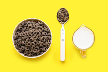 Bowl with black cereal rings and jug of milk on yellow background