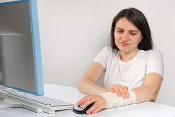 Fototapeta premium A woman with an elastic bandage on her wrist sits in front of a computer, carpal tunnel syndrome