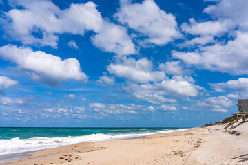 Deserted beach in Florida in stormy sunny weather. Green waves of the ocean, a piercing blue sky with lush white clouds