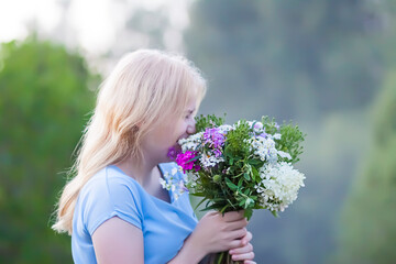 Beautiful young girl in blue dress holding the bouquet of wildflowers in her hands. 