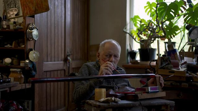 Elderly male master works in his workshop restoring japanese sword