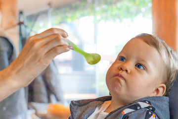 White Caucasian baby refuses to eat with a spoon in a restaurant, sitting on a high chair