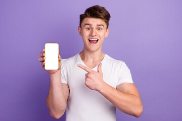 Excited guy in casual wear pointing at cellphone with empty screen on studio background space for website mobile app design