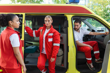 Fototapeta na wymiar Paramedics and doctor standing on the side ambulance. Doctor is carrying a medical trauma bag. Group of three paramedics standing in front of ambulance with smile.