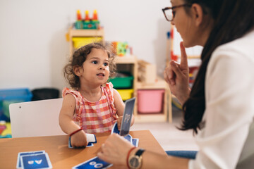 teacher and girl in kindergarten, learning how to correct pronouncing words