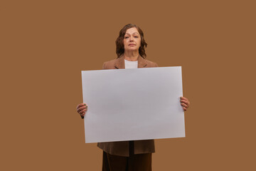 Senior woman with blank advertising board, white paper over beige studio background