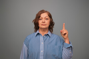 Portrait of senior friendly woman point finger empty space promoting product isolated on grey color background