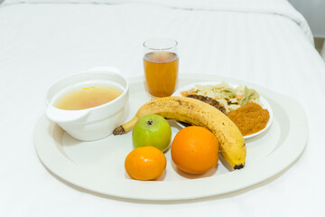 Tray with food on bed in light room. Breakfast or dinner on a tray. Soup, pasta, fruit and juice. The concept of hotel or hospital food