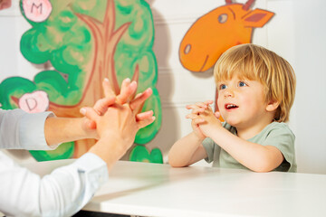 Cute blond boy play finger game sitting by the desk in class