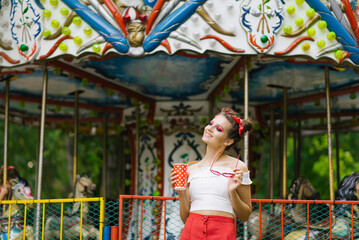 A beautiful young woman walks in an amusement park and holds a paper cup in her hands