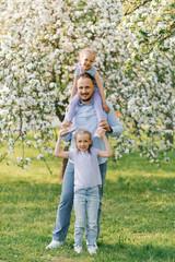 Fototapeta premium Happy young father with two daughters on a walk in the park. Portrait of a beautiful family
