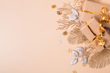 Flat lay Christmas composition from gift and twigs and leaves of golden glitter on pastel beige background. Festive shine background with empty copy space for text