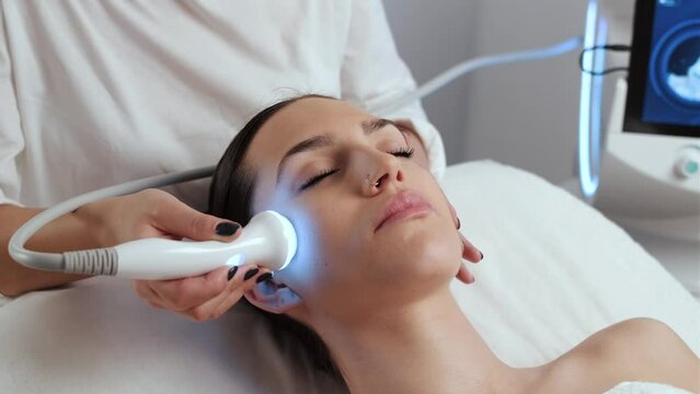 Video of cosmetologist making ultrasonic cleaning and rejuvenation the face to beautiful woman on the spa center.