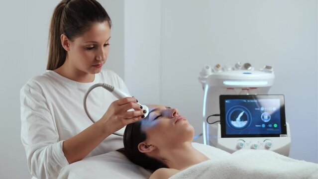 Video of cosmetologist making ultrasonic cleaning and rejuvenation the face to beautiful woman on the spa center.
