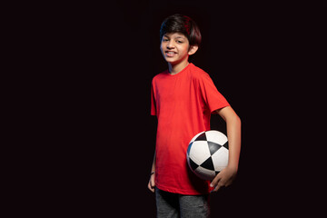 Portrait of happy boy holding football against dark background