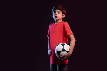 Portrait of boy holding football against dark background