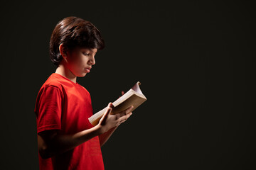 Portrait of boy reading book against dark background