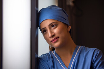 Close-up of smiling young female nurse looking through window in hospital.