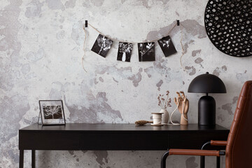 Concrete interior of home office with black desk, image, lamp and office accessories. Grey concrete wall. Home decor. Template.