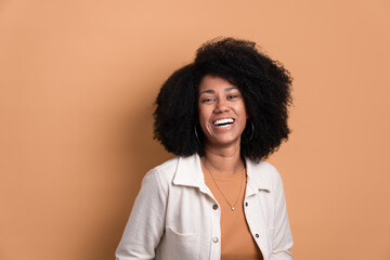 cheerful afro brazilian woman smiling and looking at camera wearing white jacket in beige studio...