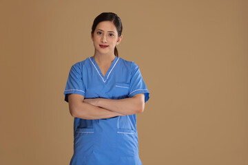 Portrait of young female nurse with hands folded against plain background