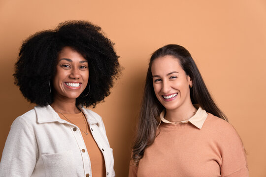 pleased two female friends smiling and looking at camera wearing white jacket in beige studio background.portrait, real people concept.