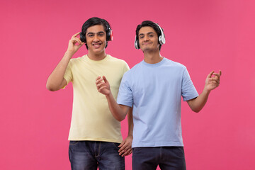 Two happy friends listening to music against pink background