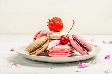 Macarons with strawberries, cherries and peonies flower petals, on a white wooden background