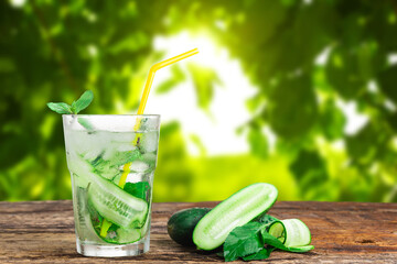 Refreshing drink with cucumber and mint, in a glass with a straw, next to ice cubes, against a green background