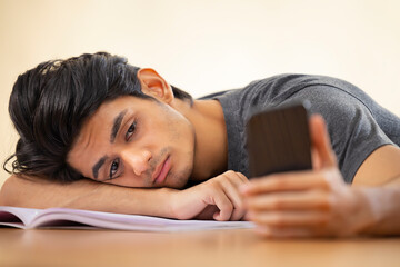 Close-up portrait of a tired teenager leaning head on hand with holding a smartphone