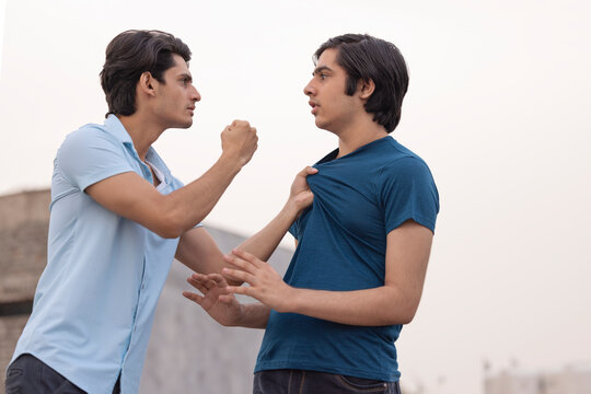 One teenage boy pulling the other by the collar of his shirt against white background