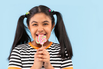Close-up of little girl biting lollipop against plain background