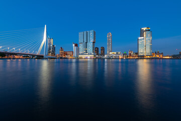 Fototapeta na wymiar Rotterdam nighttime panorama with “Erasmus-Bridge“ over river Nieuwe Maas at evening blue hour in South Holland Netherlands. Waterfront with illuminated bridge and tall buildings on the waterfront.