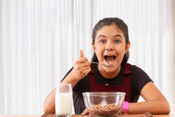 Portrait of cheerful little girl eating cereals while looking at camera 