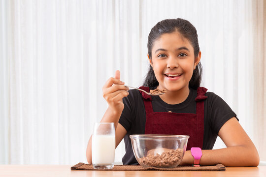 Portrait of cheerful little girl eating cereals at home 