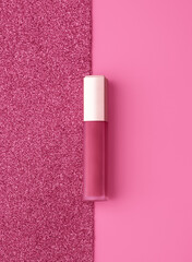 Flat lay composition with vivid pink golden lip gloss on bright pink and sparkling background....
