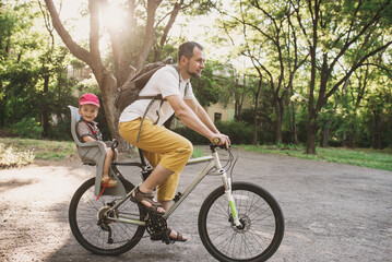 Obraz premium Dad rides his two-year-old son in a bicycle seat around the city. A man carries a small child on a bicycle. Joint vacation with children