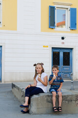 Happy family lifestyle and holiday concept. Mother, little boy, girl sitting, eating ice cream in old city, street. laughing on a summer sunny day. Having fun. Staying cool