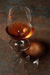 The drop of brandy falls into a broken glass.