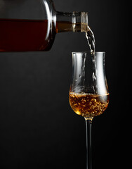 Strong alcohol drink is poured from a bottle into a glass.