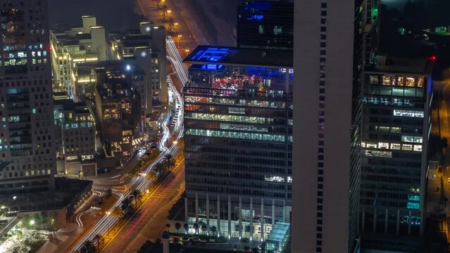 Office skyscrapers with illumination in financial district aerial during all night timelapse. Top view to hotels and traffic on a road from above with lights turning off