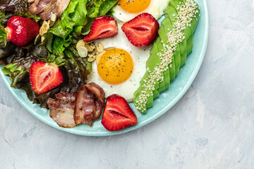 Fried egg bacon with avocado, strawberries and fresh salad. Delicious breakfast or lunch, Ketogenic, keto or paleo diet, Food recipe background. Close up