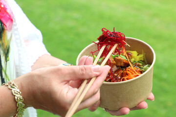 Close-up on disposable beech chopsticks with salad in a disposable kraft bowl, food takeout, tasty...