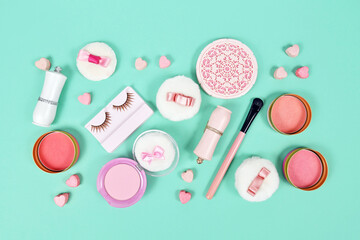 Cute pink makeup beauty products like brushes, powder or lipstick on teal blue background