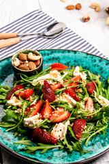 Fototapeta na wymiar Fresh strawberry salad with arugula, strawberries and cheese brie, camembert. Plate with a keto diet food. Delicious breakfast or snack on a light background, top view