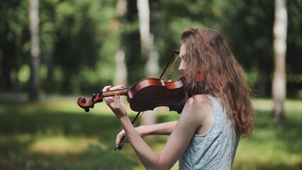 A young girl plays the violin in the city park.
