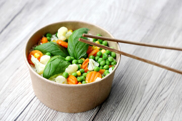 Close-up on disposable beech chopsticks with salad in a disposable kraft bowl, food takeout, tasty food - space for text