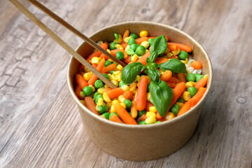 Close-up on disposable beech chopsticks with salad in a disposable kraft bowl, food takeout, tasty food - space for text