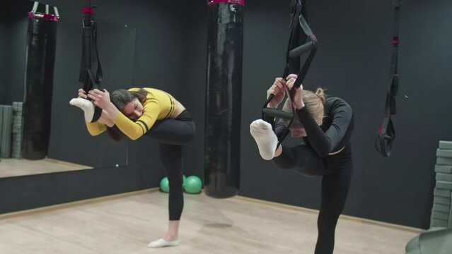 Two young Fitness women doing stretch exercise with trx fitness straps in the gym.