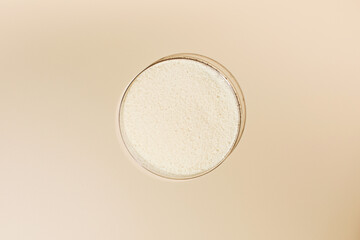 Hydrolyzed collagen powder in a Petri dish on a beige background. - obrazy, fototapety, plakaty